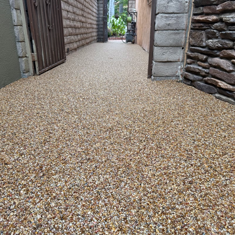 Stone carpet walkway with natural river pebbles and epoxy binder, creating a seamless, slip-resistant surface between residential walls.