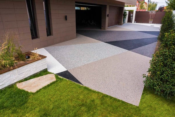 A contemporary home with a stone carpet driveway featuring a striking geometric pattern with different colored aggregates in shades of black, gray, and brown.