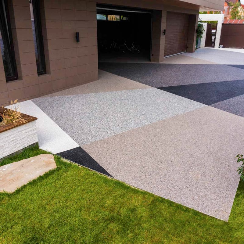A contemporary home with a stone carpet driveway featuring a striking geometric pattern with different colored aggregates in shades of black, gray, and brown.