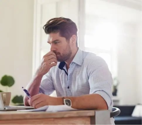 Man sitting at desk holding pen reviewing documents to help homeowner sell their property as-is for cash.