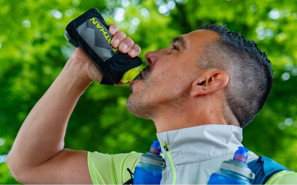 Hardloper drinkt uit Nathan waterfles om te hydrateren tijdens run.