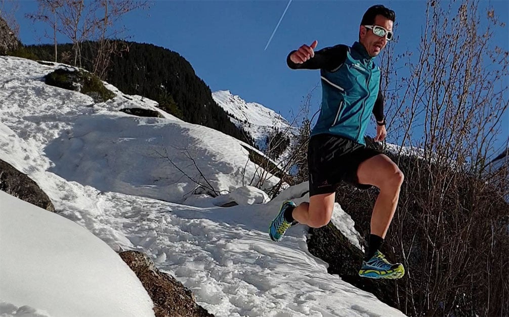 Trailrunner die in de sneeuw van een berg af springt.