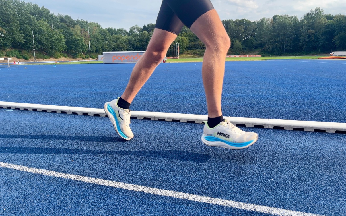 hardloper op blauwe atletiekbaan heeft hoka clifton 11 aan de voeten