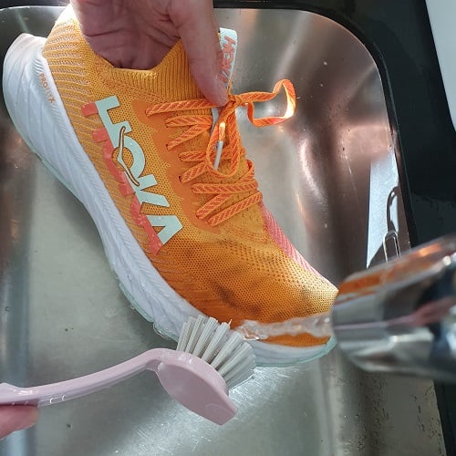 Schoonmaken vieze hardloopschoenen met borstel en water uit de kraan.