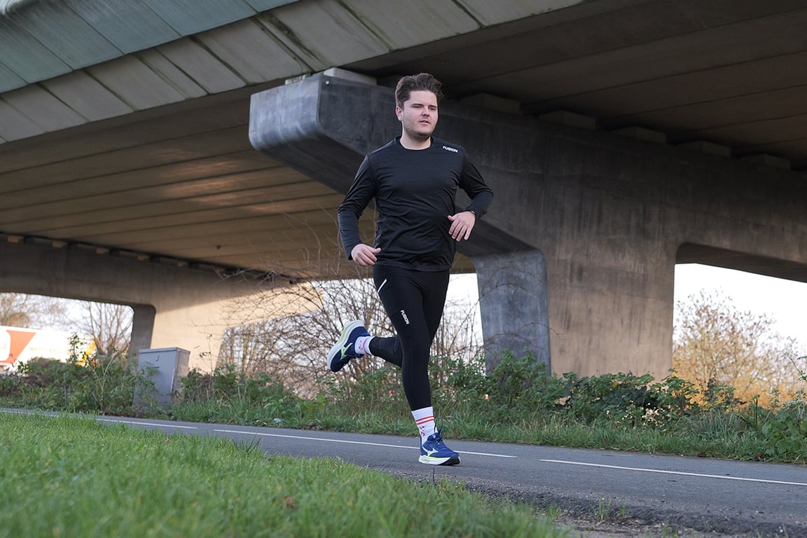 Hardloper onder brug loopt hard op blauwe hardloopschoenen van Mizuno