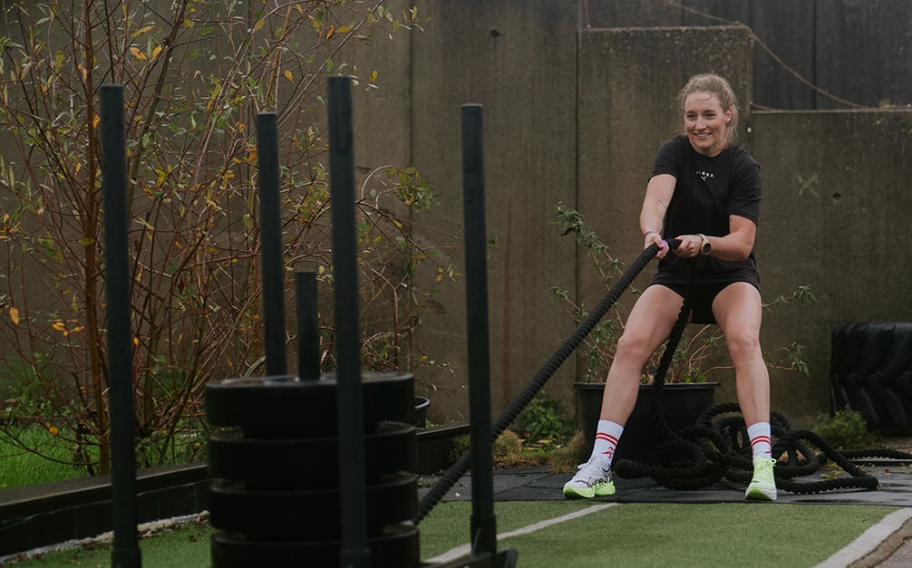 Hyrox pro dames trekt in training de sled pull over een baan.