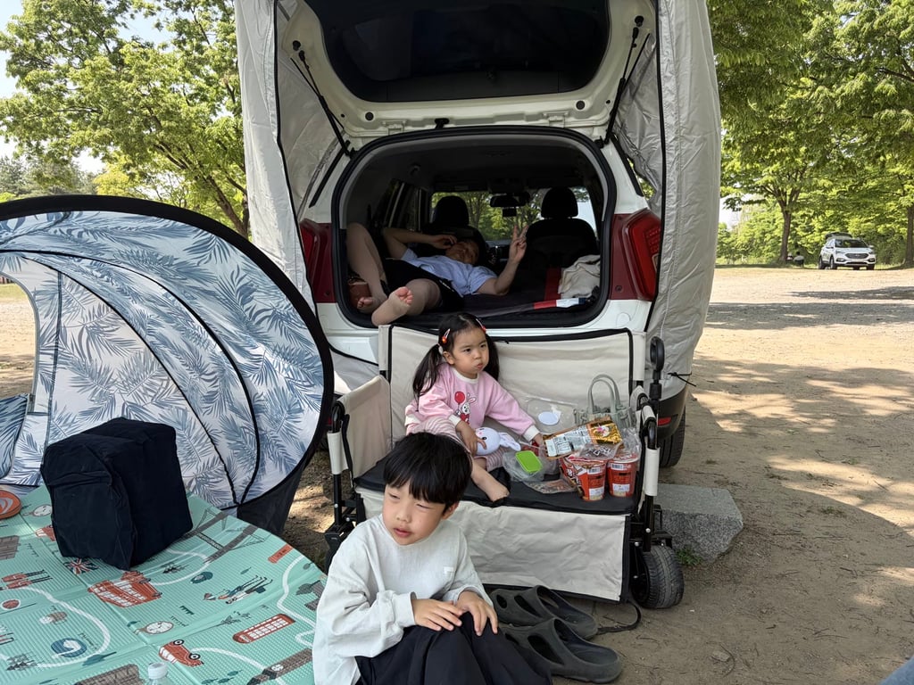 미사경정공원 차크닉 셋업 — 차 트렁크에 오빠가 누워 있고 동생은 의자에서 간식 먹는 모습