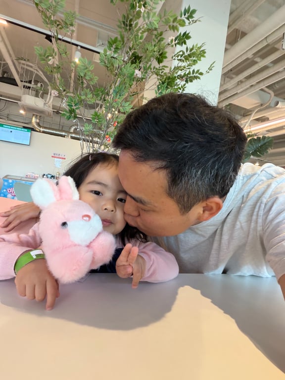 쥬라리움 하남점 카페에서 아빠가 아이 볼에 뽀뽀하며 핑크 토끼 인형과 함께 찍은 가족 사진