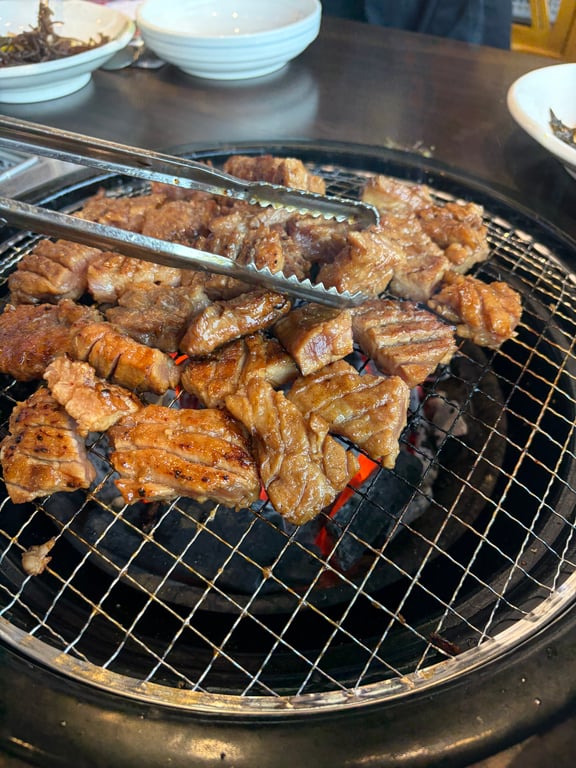 훈장골 하남점 잘 구워진 돼지갈비 조각 집게로 잡은 클로즈업