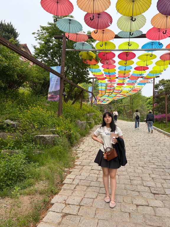 허브아일랜드 우산 포토존 — 알록달록 색깔 우산들 아래 거리에 서 있는 엄마