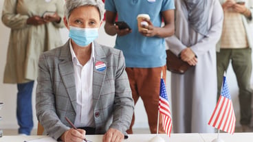 Multi-ethnic group of people standing in row and wearing masks at polling station on election day, focus on modern senior woman  while registering for voting, copy space