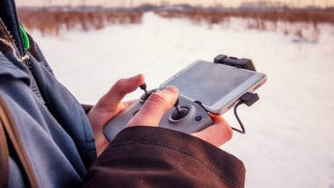 Caucasian Male in the blue jacket launching a flying drone with a remote controller in his hand on winter field.