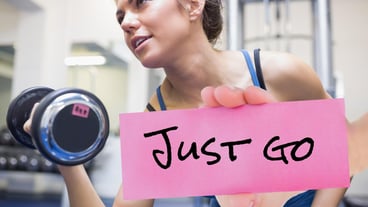Hand holding placard with text just go and woman exercising with dumbbell in background