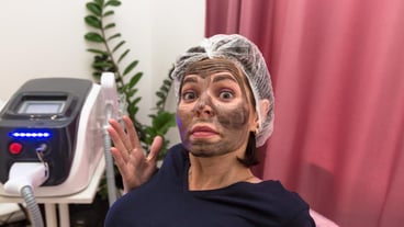 Woman with face smeared with carbon mask in beauty salon