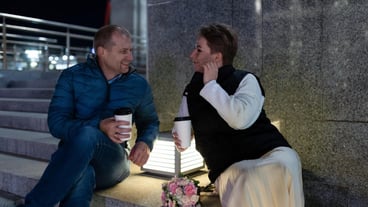 A couple sits on steps in the city at night enjoying a warm drink