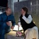 A couple sits on steps in the city at night enjoying a warm drink