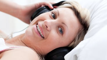 Positive woman with headphones lying on a bed