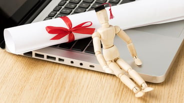 High angle laptop with wooden figurine and academic hat