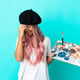 Young mixed race woman with pink hair holding a palette isolated on blue background laughing