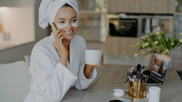 smiling woman with hydrogel spots under her eyes enjoying a hot tea while talking on the phone