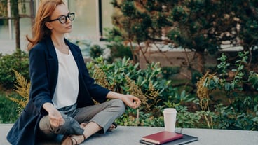 Calm redhaired woman relaxing meditating while working remotely on laptop outdoors