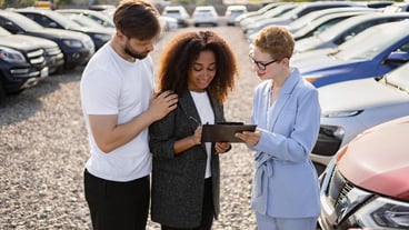 A couple signs paperwork with a car salesperson in a dealership potentially finalizing a vehicle