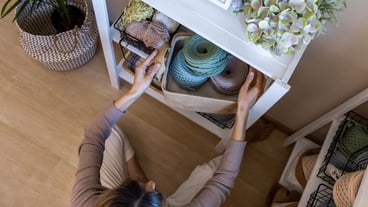 Top view woman knitted clothing and accessories designer tidying up ribbon yarn sticks closet storage organization Creative female art craft hobby or work placing details on shelves filling cabinet