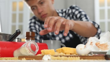 Upset man with many dirty dishware utensils and food leftovers on table in messy kitchen selective focus