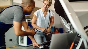 Happy woman talking to her car mechanic in a repair shop