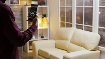 Young man uses a smart light app to turn on the lights in the house then he sitts on the sofa
