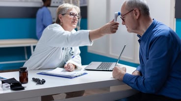 Specialist using a thermometer to measure the temperature of a sick man, checking for medical attention and flu symptoms. Doctor measuring the patient's fever using medical instruments during an annual check-up.