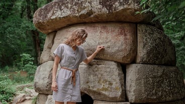 Young woman in summer dress walking near big dolmen stone in the forest