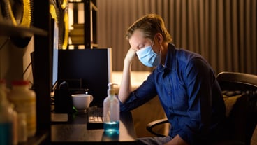 Stressed young businessman with mask looking tired while working from home late at night
