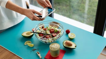 Female hands taking photo of a bowl with salad and half of avocado
