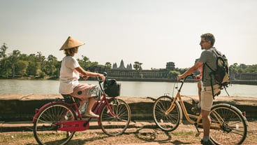 Tourist couple cycling in Angkor temple, Cambodia. Angkor Wat main facade reflected on water pond. Eco friendly tourism traveling. Toned