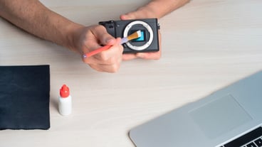 Person cleaning mirrorless digital camera sensor with swab and lens.