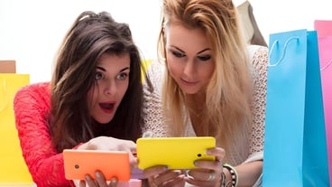Friends compare purchases and share excitement over a shopping spree smartphones in hand