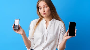 Young woman holding old and new phone on blue background.