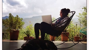 Woman working on laptop against cloudy sky by dog