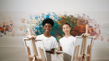 African boy and caucasian girl look at camera while paint canvas edification