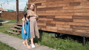 Young pregnant mother talking with her little daughter while they walking outdoors