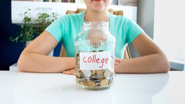 Close up portrait of young lady in T-shirt sitting at the white table on which is located ,full of coins, jar with the inscription credit