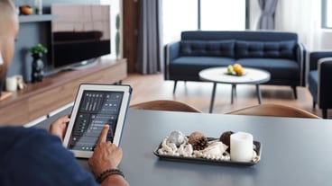 Man sitting at table and using smart home application on digital teblet when dimming lights in the room