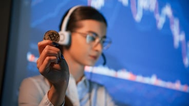Holding bitcoin in hand Female stock broker is working indoors Big wide display behind her