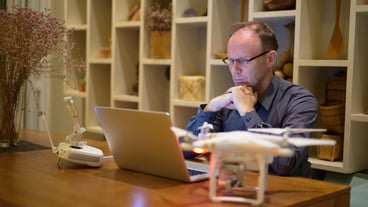 Mature man with drone and laptop in the dining room at home