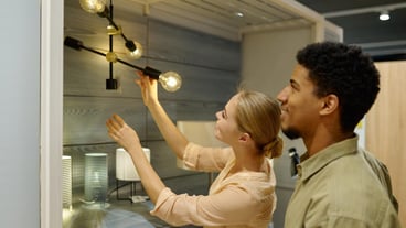 Smiling couple of customers choosing a chandelier in a furniture store. Woman touching modern design chandelier