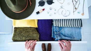 Woman choosing outfit from drawer dresser with stylish casual trendy clothes, home stuff and female accessories. Top view.