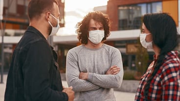 Friends in masks meeting on city street