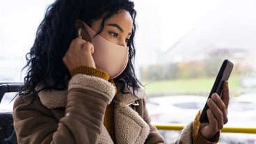 Woman wearing medical mask in the bus while listening to music in earbuds