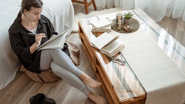 A young female student does assignments at home, sitting with a notebook in her hands.
